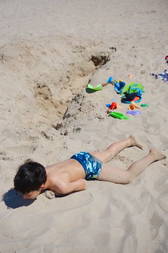 Young boy playing with sand at a beach on a sunny day.