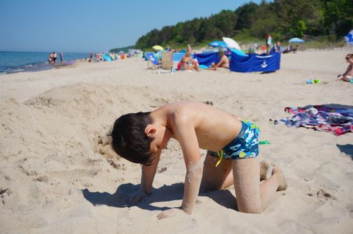 Young boy playing with sand at a beach on a sunny day.