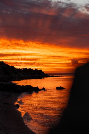 Sun setting over ocean beach with rocks in water