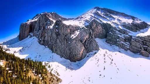 A scenic view of a rocky mountain covered with white snow during winter