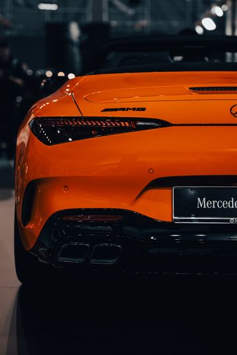 A vertical shot of the back side of an orange luxury Mercedes-Benz AMG SL with blur background