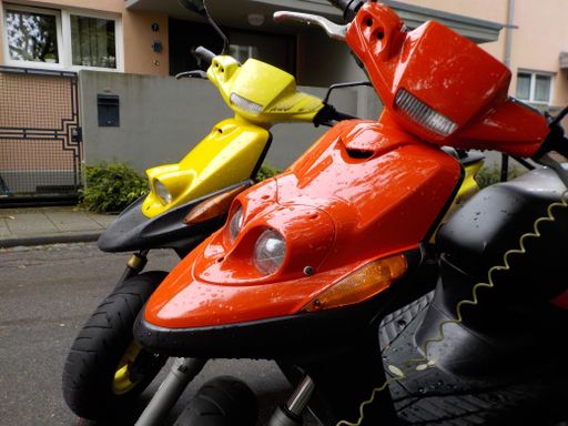 The yellow and red platic front skirts of two motor scooters with raindrops make a gloomy day seem colourful.