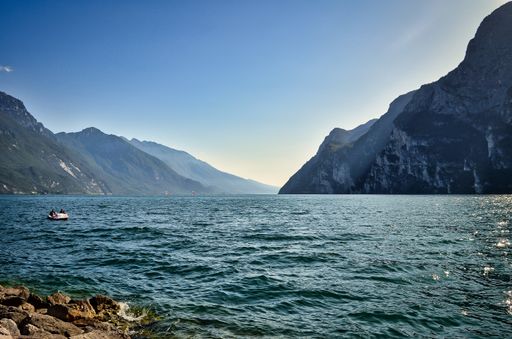 landscape photo of the beautiful evening view from Riva del Garda / Torbole to the south lake with mountains, cliffs, blue sky, boat