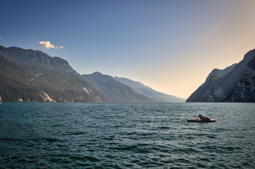 landscape photo of the beautiful evening view from Riva del Garda / Torbole to the south lake with mountains, cliffs, blue sky, sunset, boat
