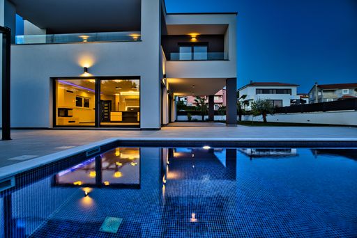 A contemporary villa with a pool and terrace in evening twilight.