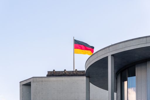 The flag of Germany on a pole flying over a building in Berlin, Germany against a cloudy sky