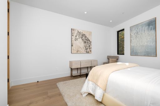 A ved and desk in a bedroom by a window with the artwork.
