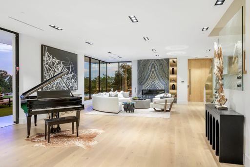 A room with a grand piano, sofas, and expansive windows.