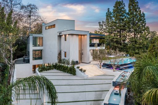 A luxurious white house with a pool, surrounded by trees, during sunset.