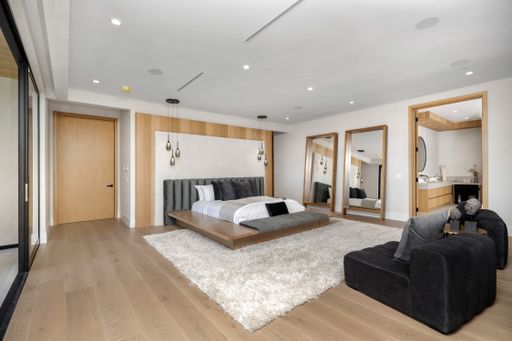 A spacious bedroom with wooden floors, a large bed, and a black leather armchair.