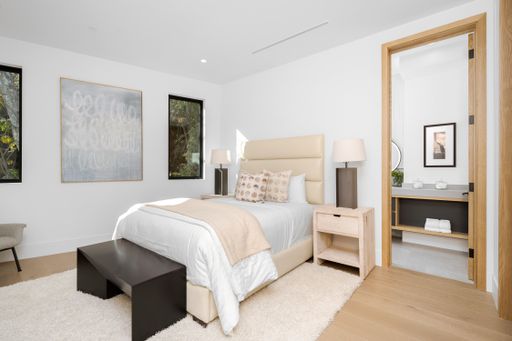 A bedroom with a white bed and dresser by a window.