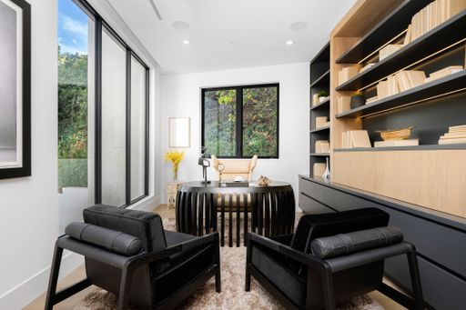 A living room with two sofas, armchairs, and an open bookcase.