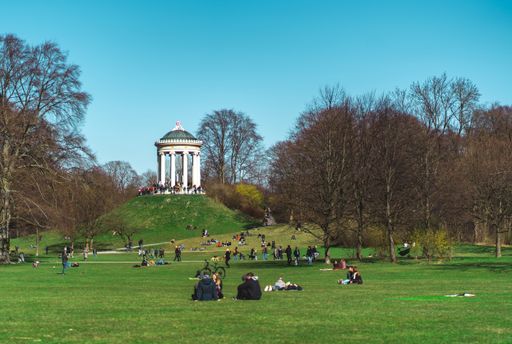 Friends sitting in the English Garden (Englischer Garten) in Munich on a beautiful sunny day in winter. Monopterus in the background