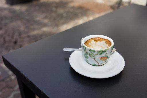 A selective focus of a coffee latte in a floral detailed cup and white saucer