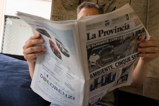 adult caucasian italian man reading newspaper outdoors wearing summer clothing