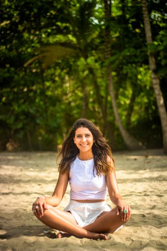A young Hispanic female in a white dress performing yoga on the beach