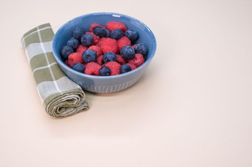 A bowl of fresh blueberries and raspberries isolated on a light background with space for text