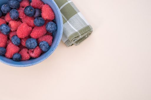 A bowl of fresh blueberries and raspberries isolated on a light background with space for text