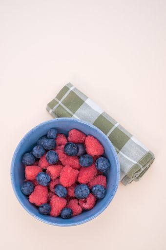A vertical shot of a bowl of fresh blueberries and raspberries isolated on a light background