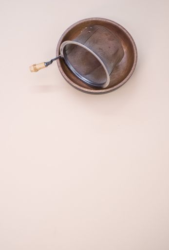 A vertical shot of a tea strainer on a plate isolated on light pink background