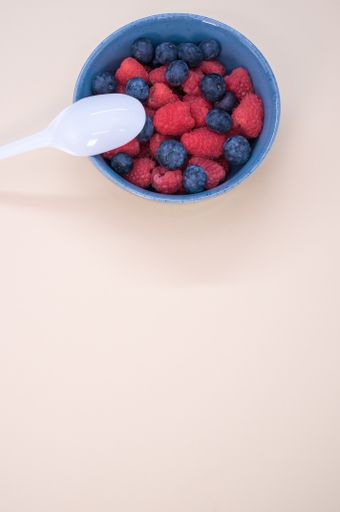 A vertical shot of a bowl of fresh berries with a plastic spoon isolated on a light background