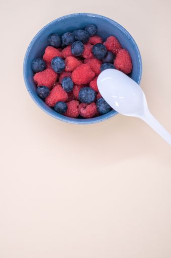 A vertical shot of a bowl of fresh berries with a plastic spoon isolated on a light background
