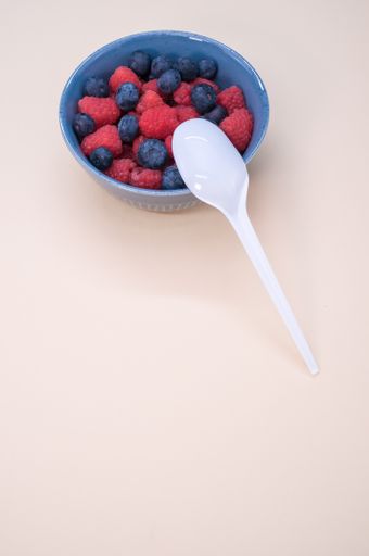 A vertical shot of a bowl of fresh berries and plastic spoon isolated on a light background