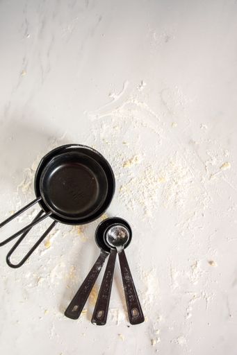 Various kitchen tools and two pans on flour surface
