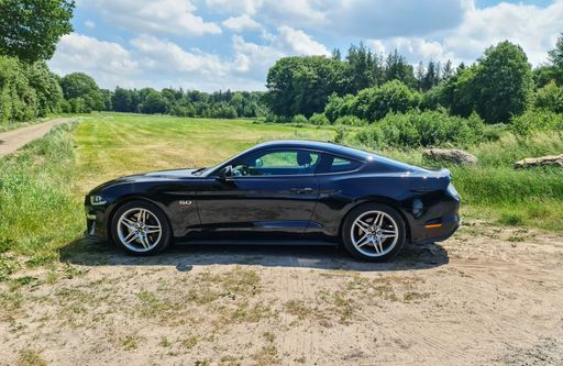 Side view on a black Ford Mustang Model 2018 in front of a northern germany landscape