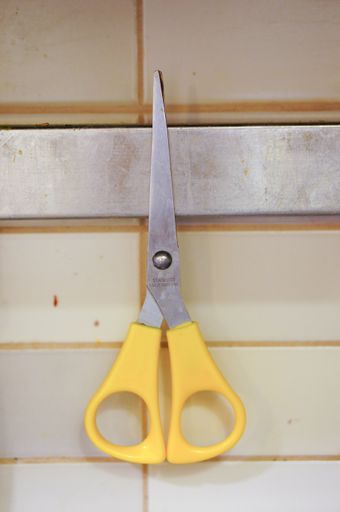 A vertical shot of a yellow scissor attached to a magnet
