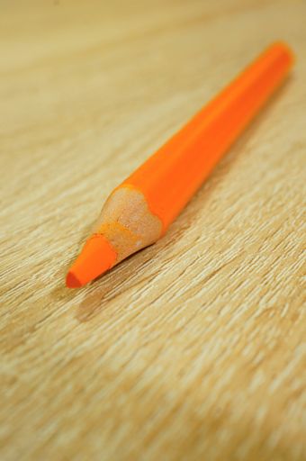 A vertical shot of an orange drawing pencil on a wooden surface