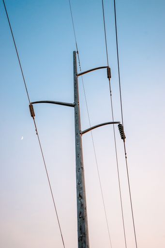 A vertical shot of wires and a transmission tower in the evening