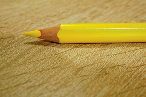 A closeup shot of a yellow drawing pencil on a wooden surface