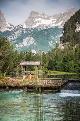 A vertical shot of a small dam over a river surrounded by greenery under the sunlight