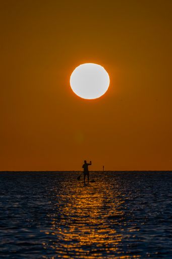 a person surfing at sunset silhouetted against the setting sun