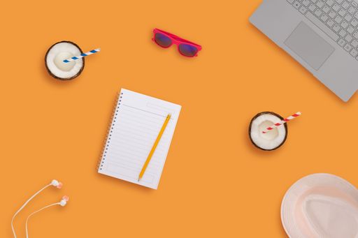 A top view of an orange office desk with coconut sunglasses headphone laptop white hat.