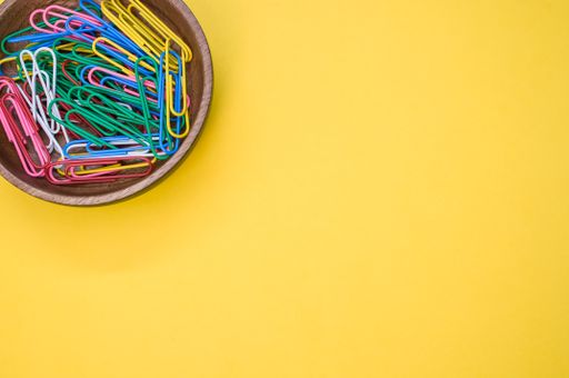 A closeupshot of multi-colored paper clips on a yellow surface - copy space