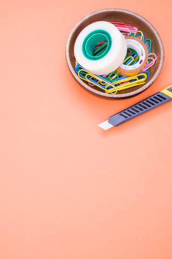 A vertical shot of multi-colored paper clips and duct tape on an orange surface - copy space