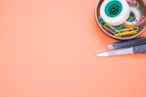 A closeup shot of multi-colored paper clips and duct tape on an orange surface - copy space