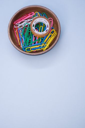 A vertical shot of multi-colored paper clips and duct tape on a blue surface - copy space