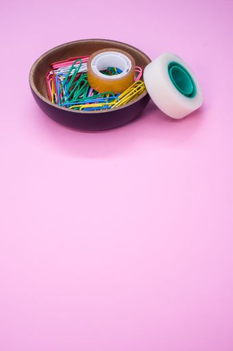 A vertical shot of multi-colored paper clips and duct tape on a pink surface - copy space
