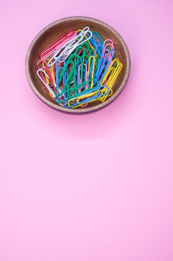 A vertical shot of multi-colored paper clips on a pink surface - copy space