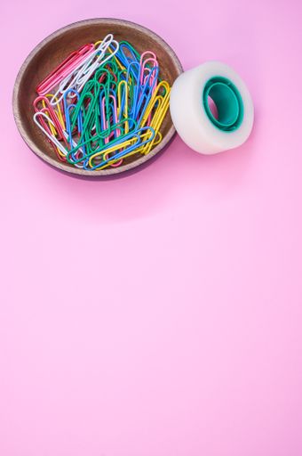 A vertical shot of multi-colored paper clips and duct tape on a pink surface - copy space