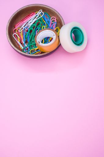 A vertical shot of multi-colored paper clips and duct tape on a pink surface - copy space
