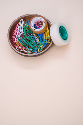 A vertical shot of colorful paper clips and adhesive tapes in a wooden bowl