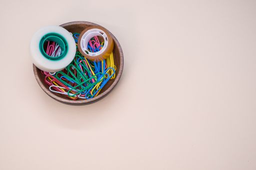 A top view of multi-colored paper clips and duct tape on a beige surface - copy space