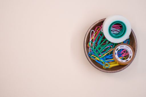 A top view of colorful paper clips and adhesive tapes in a wooden bowl