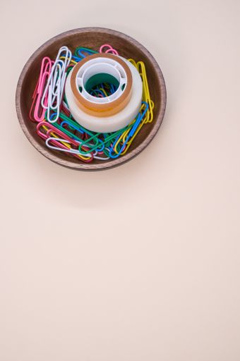 A vertical shot of multi-colored paper clips and duct tape on a beige surface - copy space