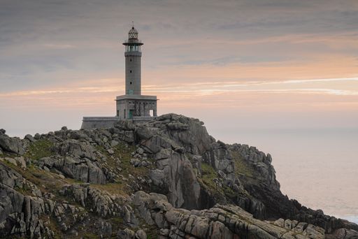 A scenic view of the famous Punta Nariga lighthouse in Galicia, Spain against a beautiful sunset