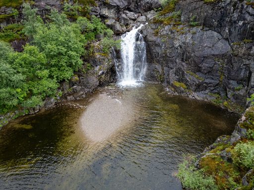 An aerial view of a scenic flowing waterfall near a lush forest in Norway